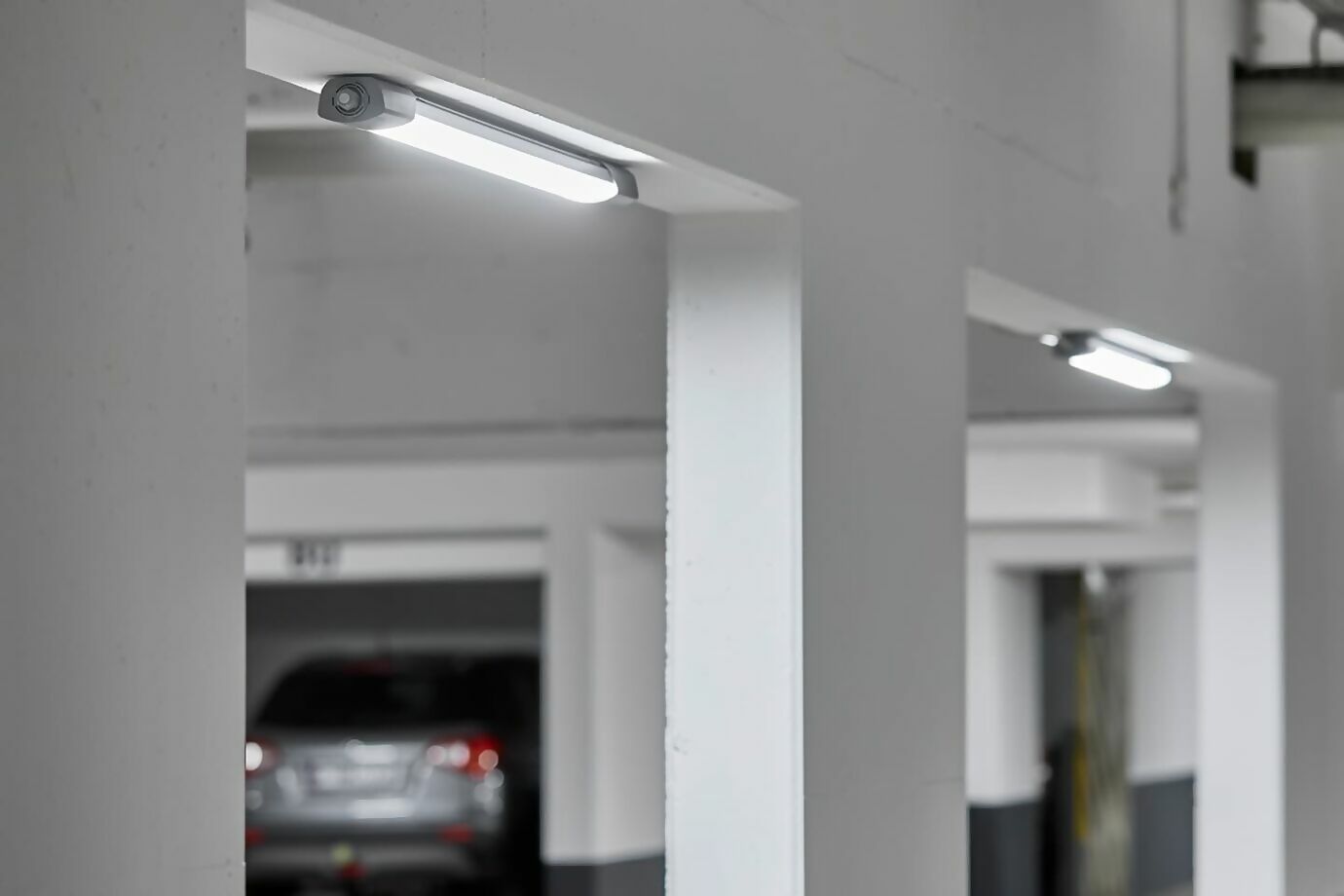 Lampes LED à capteur dans un parking souterrain avec une voiture garée en arrière-plan