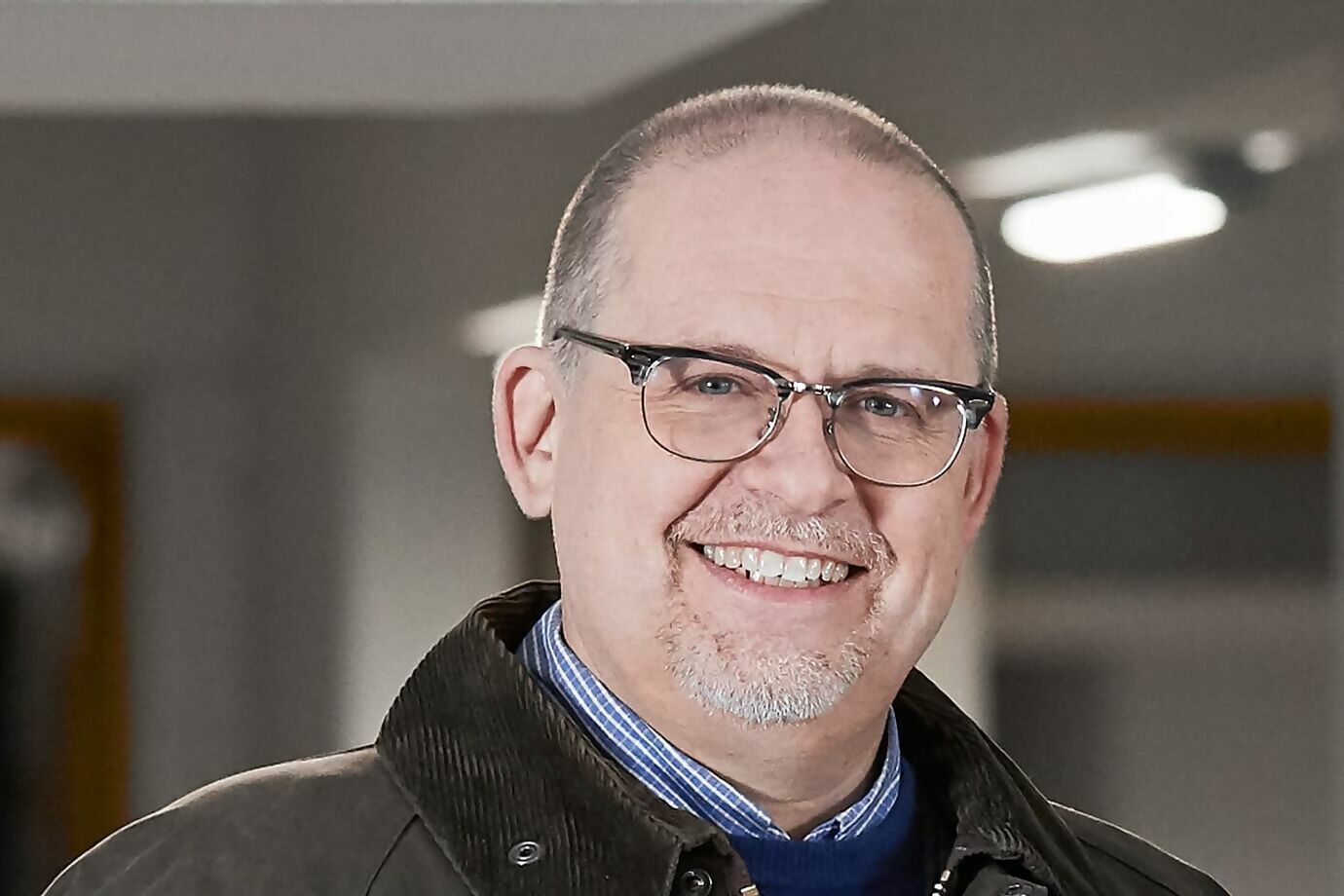 Portrait d'un homme souriant avec des lunettes devant un arrière-plan flou.