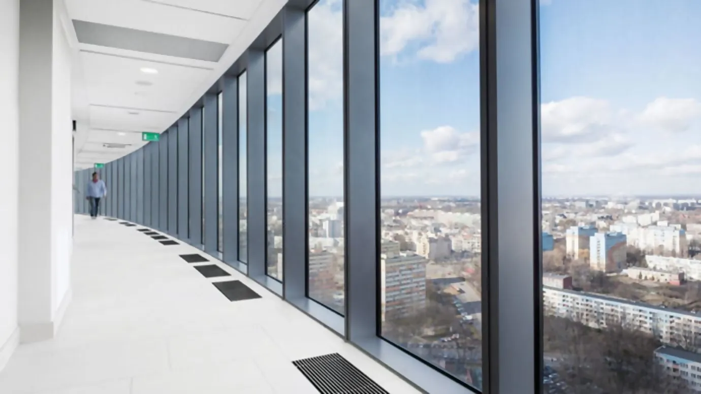 Corridor with a white wall on the left and a glass front on the right with a view of the city