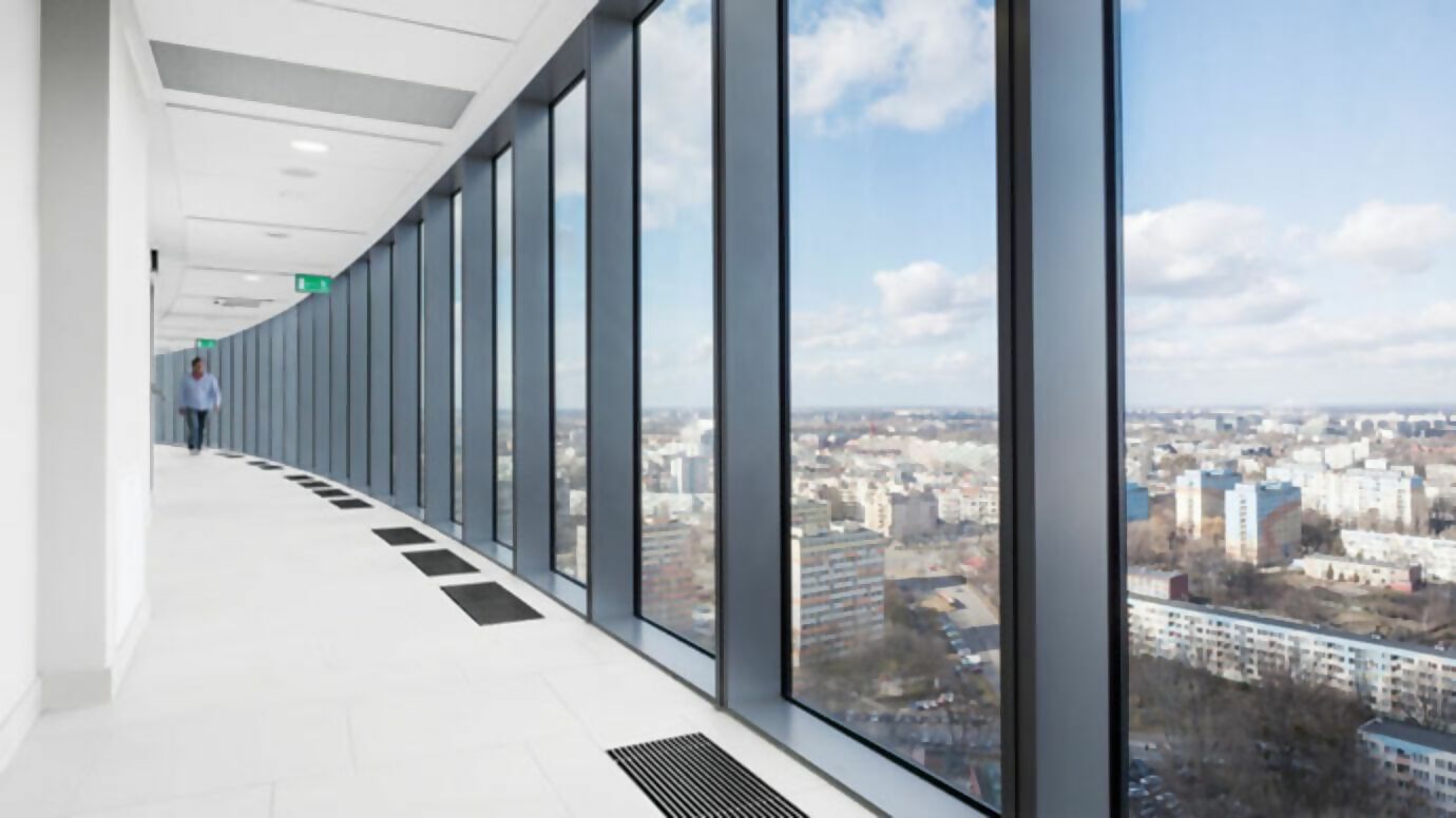 Korridor mit weißer Wand auf der linken Seite und Glasfront auf der rechten mit Ausblick auf Stadt