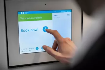 Display auf dem steht "Book now", wo gerade jemand drauftippt
