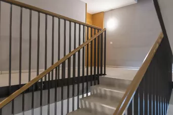 Modernes Treppenhaus mit Metallgeländer, Holzhandlauf und beleuchteter Wand in einem Wohngebäude.