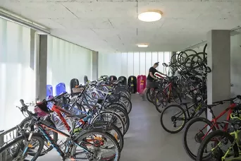 Fahrradraum mit zahlreichen abgestellten Fahrrädern, Wandhalterungen und moderner Deckenbeleuchtung.